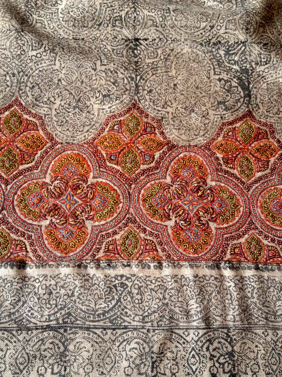 A shawl border half embroidered in coral and ochre, the rest still showing the printed outline.
