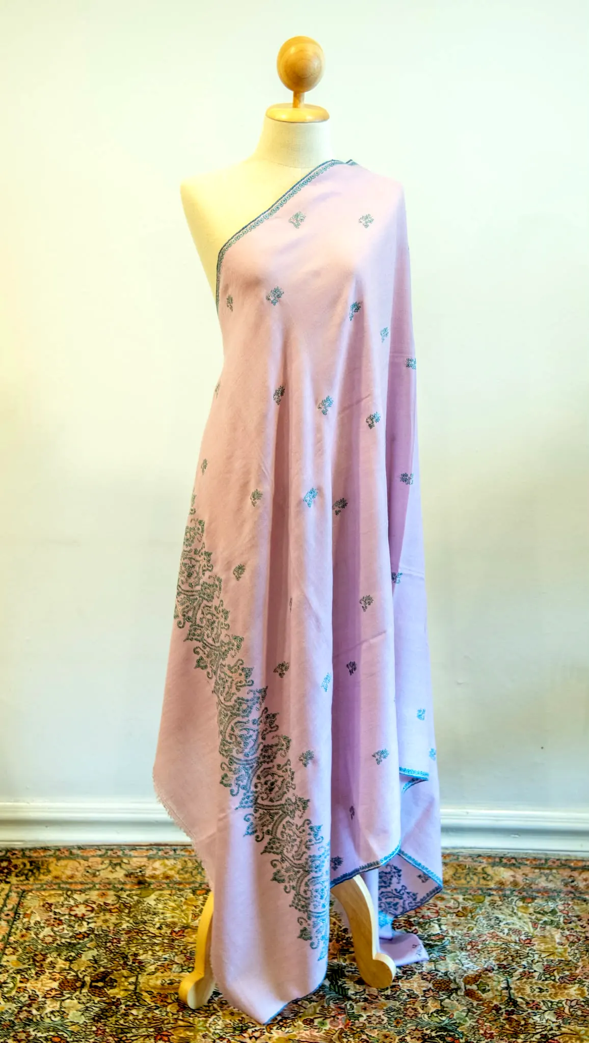 Pale pink shawl with scattered needlework sprigs and a worked end, draped on a stand.
