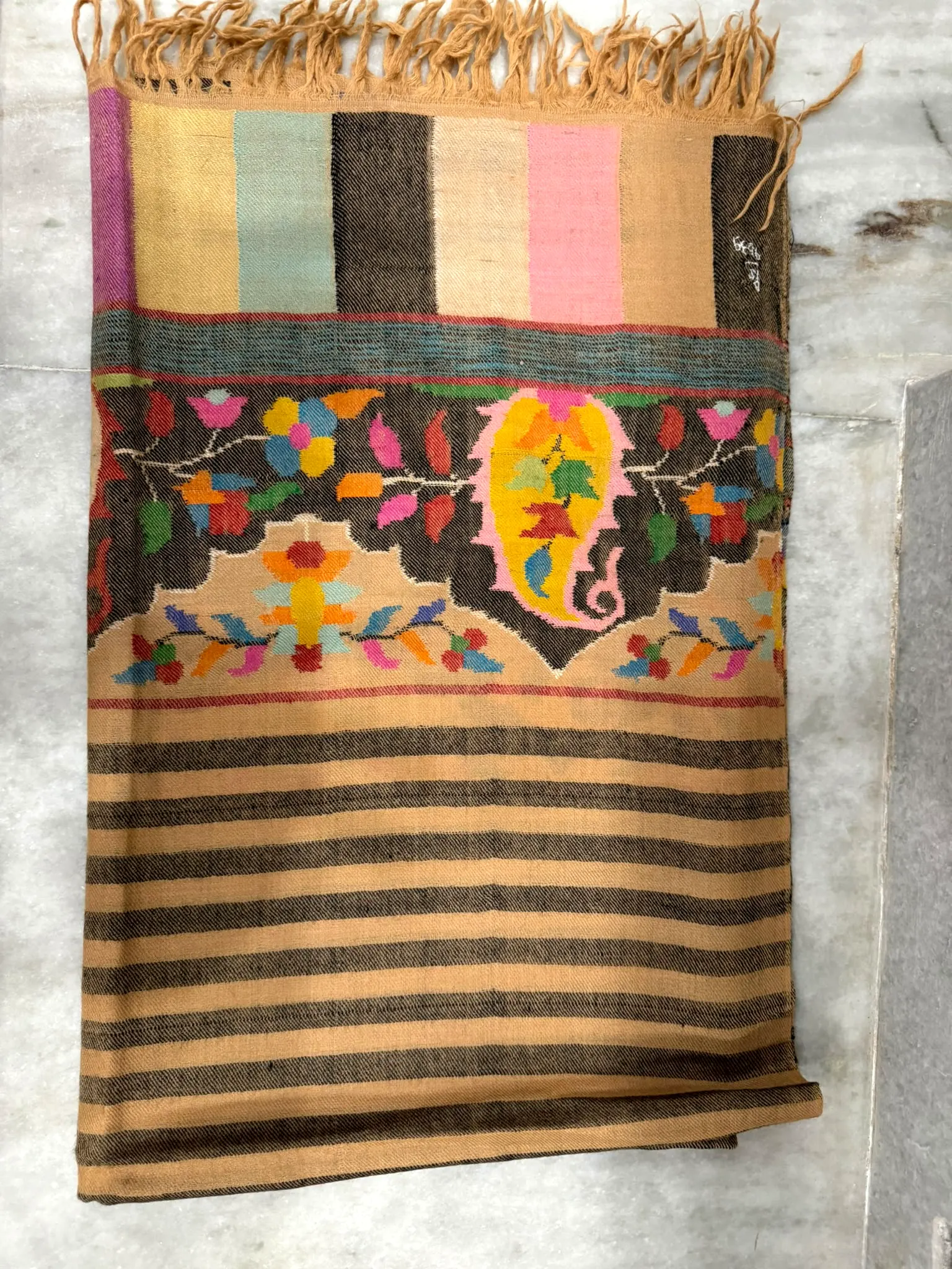 Kani shawl laid flat with camel and black stripes, a floral band with a yellow paisley, and a fringed end.