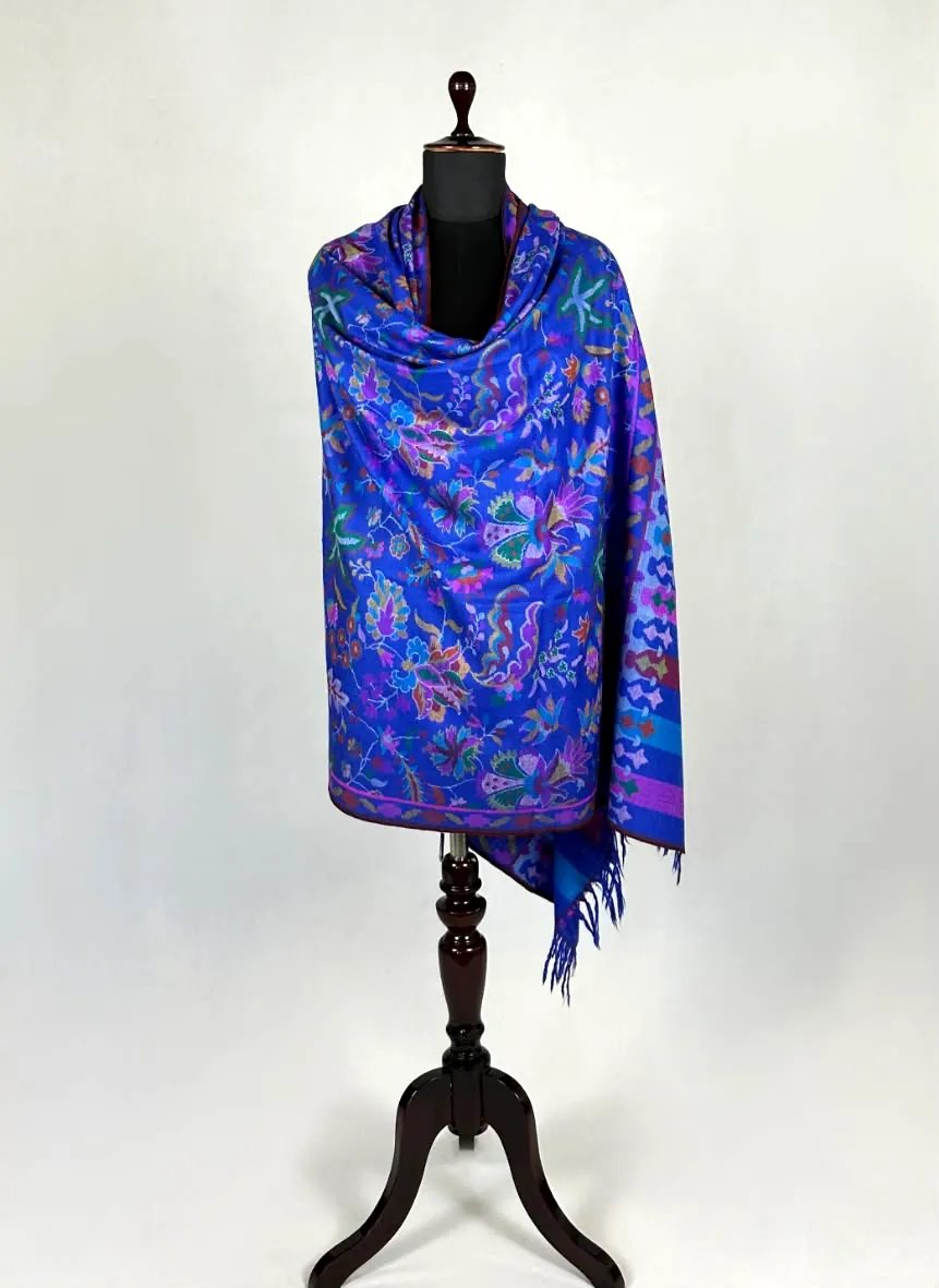 Cobalt blue kani shawl patterned with green, pink and violet flowers, draped on a dark wooden stand.