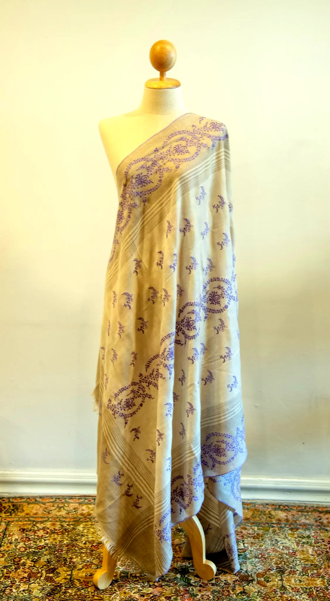 Pale gold shawl with lilac needlework motifs and border, draped on a stand.