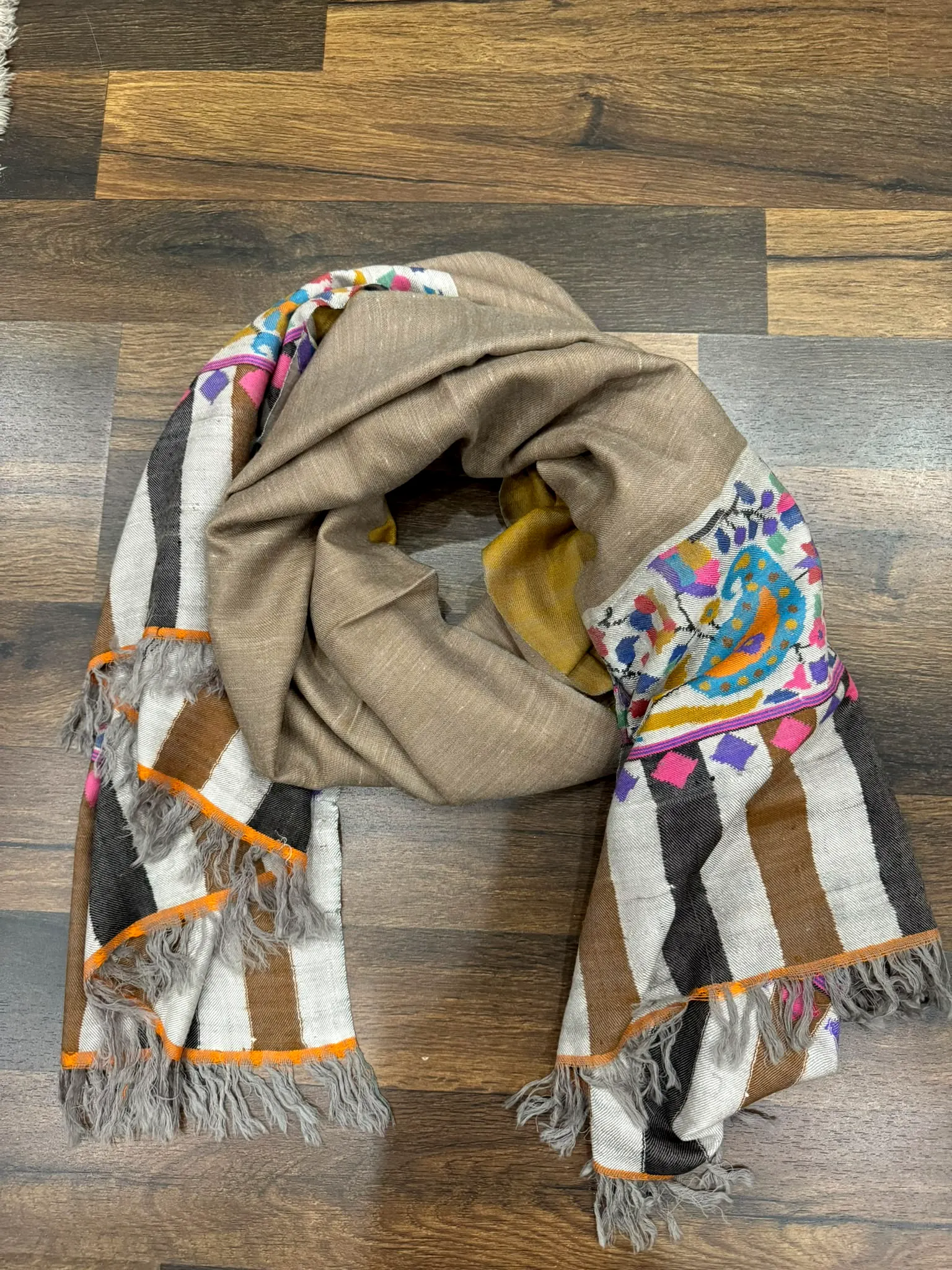 Plain mushroom kani stole with woven floral and striped ends, on a wooden floor.