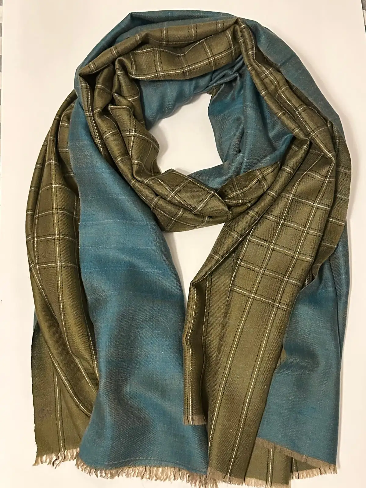 Reversible stole with an olive check on one face and plain blue on the other, coiled on a white surface.