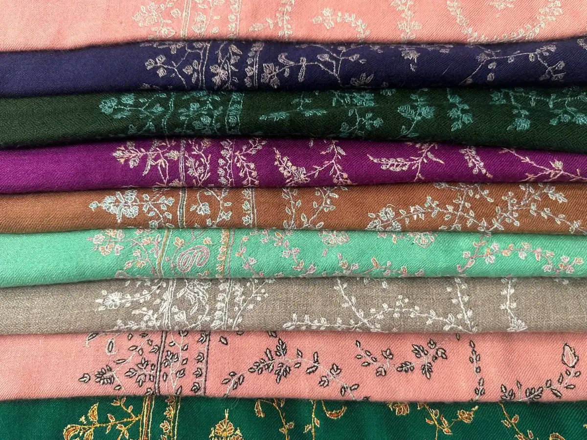Stack of folded sozni stoles in pink, navy, green, plum, rust, mint, taupe and emerald, each with fine embroidered sprigs.